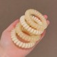 Four translucent cream-colored spiral phone cord hair ties held in a person's hand against a solid taupe background.