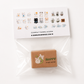 A clear plastic bag containing a small brown rectangular box with a cute bunny illustration and the word HAPPY, sealed under a printed card showing multiple small character designs and the text BubbleGumFringe.com.